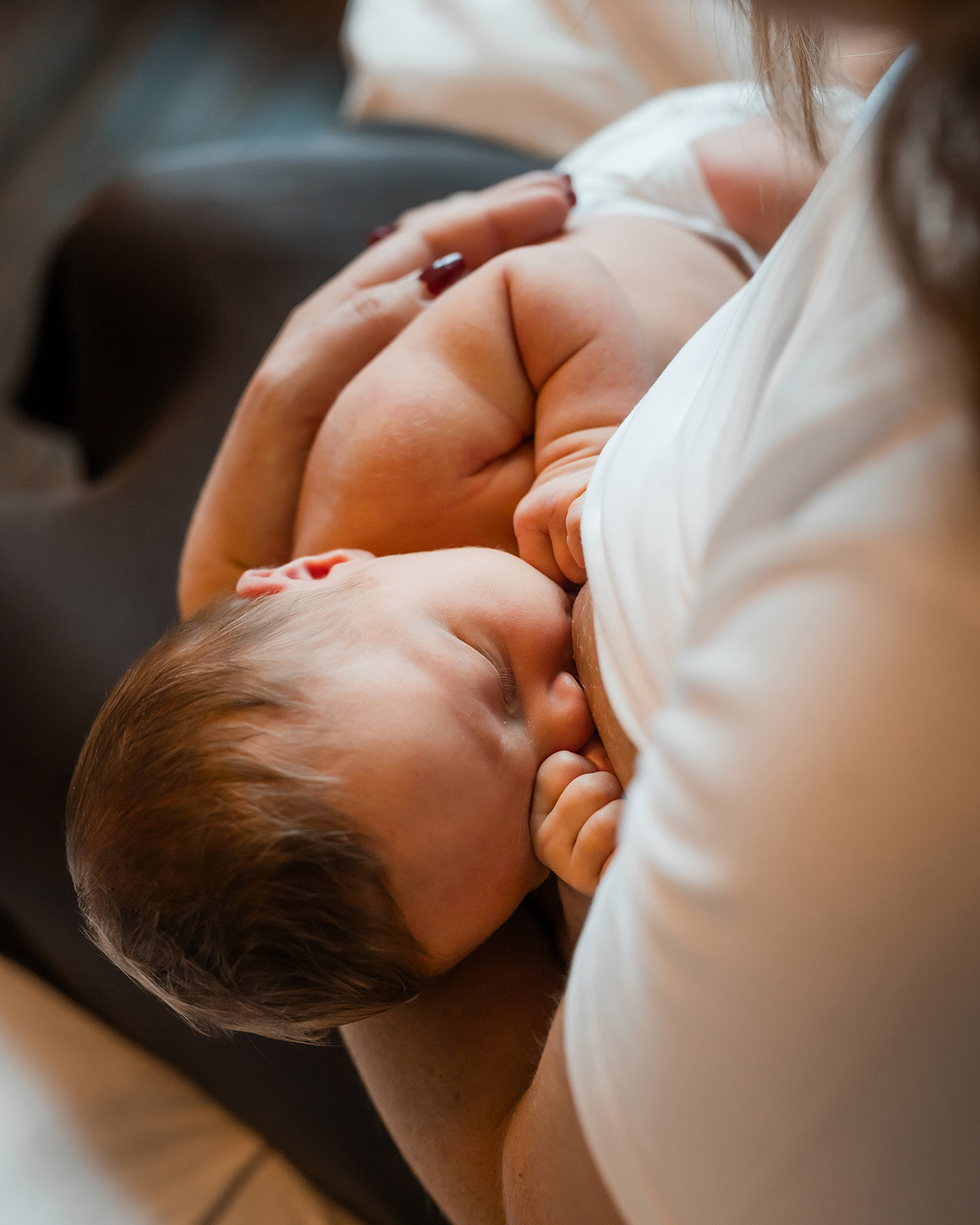 Ett barn med brunt hår ammar och vaggas i en vuxens famn. Den vuxne bär en vit skjorta och håller barnet nära sig i en vårdande position. Scenen verkar lugn och intim.